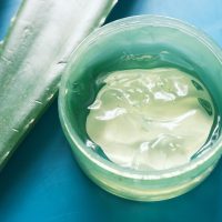 Fresh aloe vera sliced and liquid gel in plastic container on green background Fresh aloe vera sliced and liquid gel in plastic container on green background .